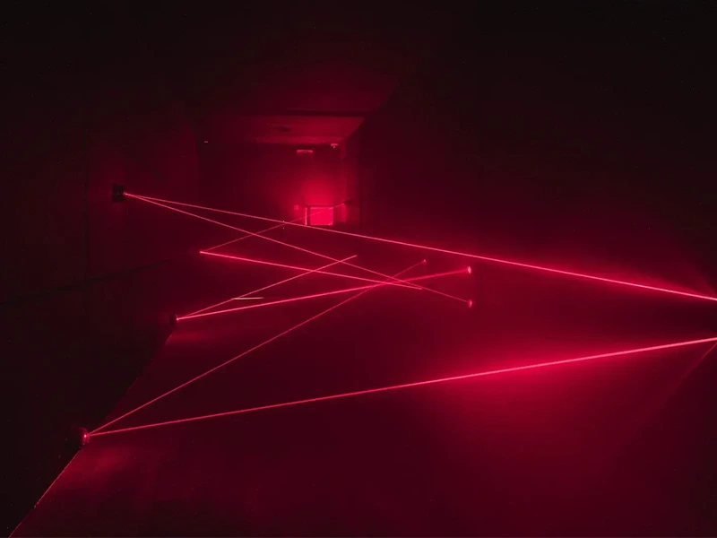 Rote Laserstrahlen kreuzen sich in einem dunklen Raum und erzeugen faszinierende Lichtmuster. Ideal für Lichtshows.
