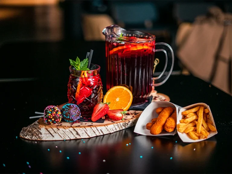 Erfrischender Cocktail in einer Karaffe, serviert mit bunten Snacks und Pommes auf einem stilvollen Tisch.