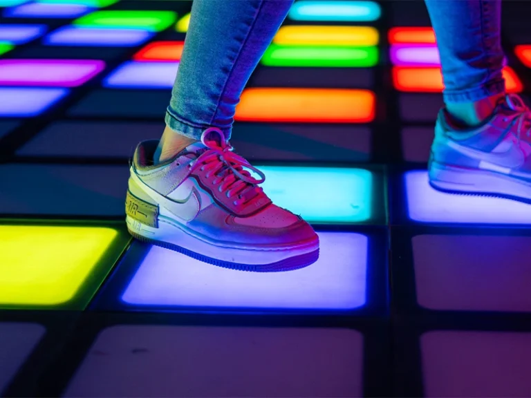 Person trägt modische Sneaker auf einer bunten, beleuchteten Tanzfläche. Die Farben leuchten lebhaft und ziehen Aufmerksamkeit an.