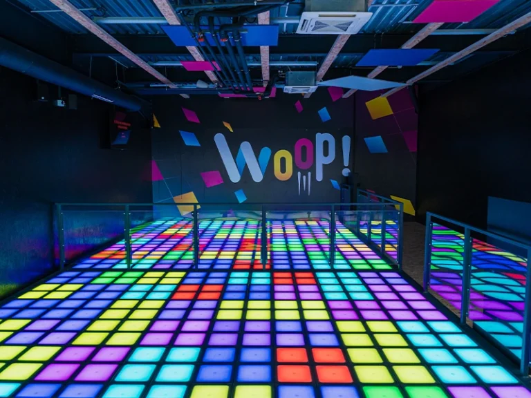 Bunte Tanzfläche in einer modernen Freizeitstätte mit dem Schriftzug "Woop!" an der Wand. Ideal für Events und Feiern.