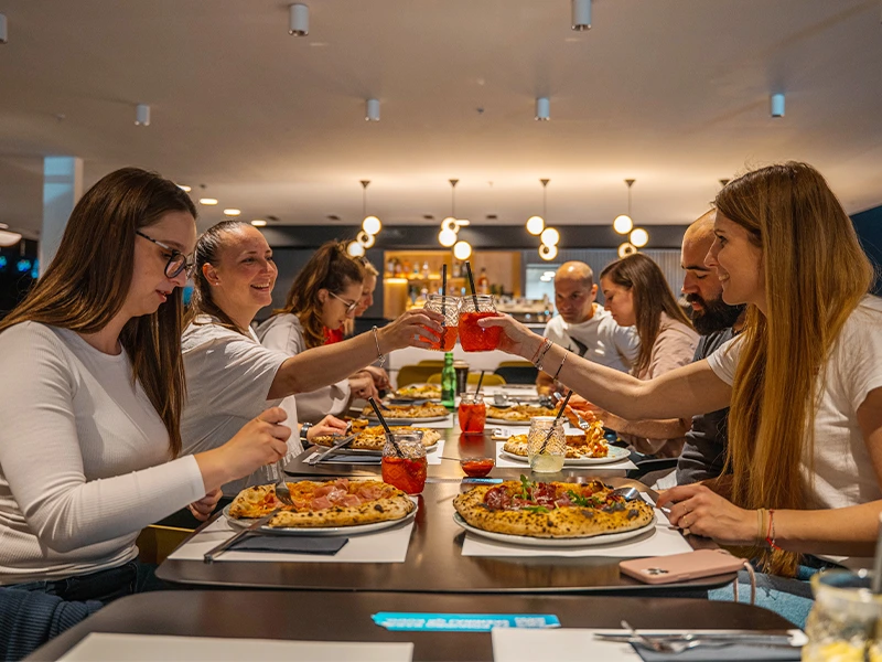 Gruppe von Freunden, die beim Essen an einem Tisch anstoßen. Leckere Gerichte und Getränke in einem modernen Restaurant.