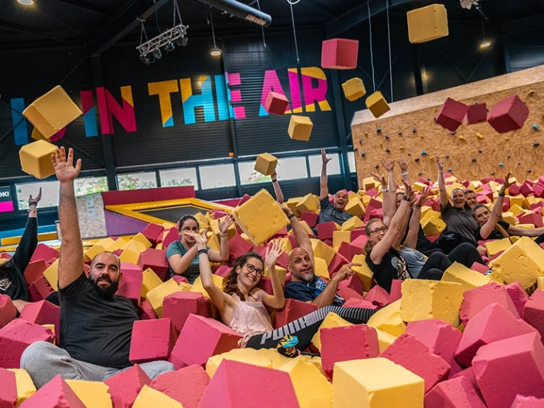 Gruppe von Menschen, die in einem Schaumstoffbecken Spaß haben. Bunte Schaumstoffwürfel fliegen durch die Luft.