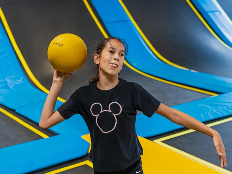 Mädchen mit einem gelben Ball in der Hand auf einem Trampolinplatz, bereit zum Spielen. Spaß und Bewegung in der Luft!