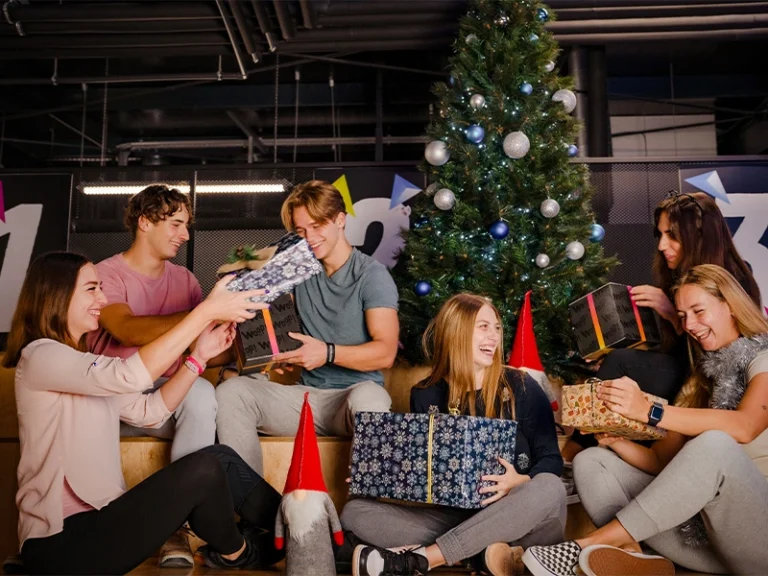 Junge Menschen feiern Weihnachten mit Geschenken und einem Weihnachtsbaum im Hintergrund. Festliche Stimmung und Freude.