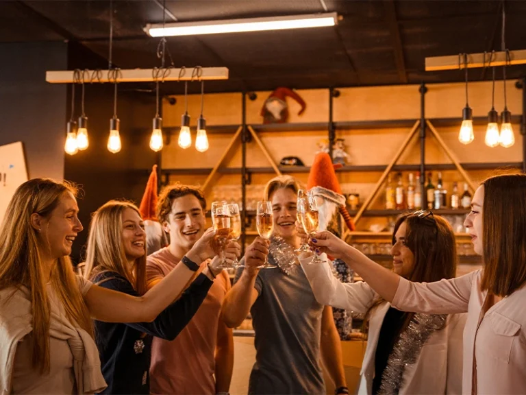 Gruppe junger Menschen stößt in einer gemütlichen Bar mit Gläsern an und feiert gemeinsam. Freundliche Atmosphäre und Freude.