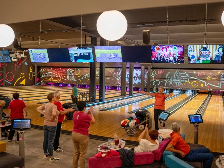 Moderne Bowlingbahn mit fröhlichen Gästen, bunten Lichtern und interaktiven Bildschirmen im Hintergrund.