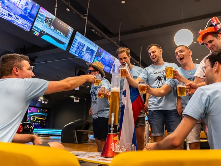 Gruppe junger Männer feiert mit Bier und Spaß in einer modernen Bowlinghalle, umgeben von Bildschirmen.