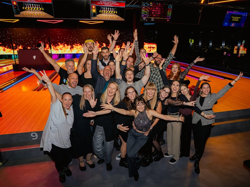 Gruppenselfie von fröhlichen Menschen beim Bowling-Event, mit buntem Hintergrund und leuchtenden Lichtern.