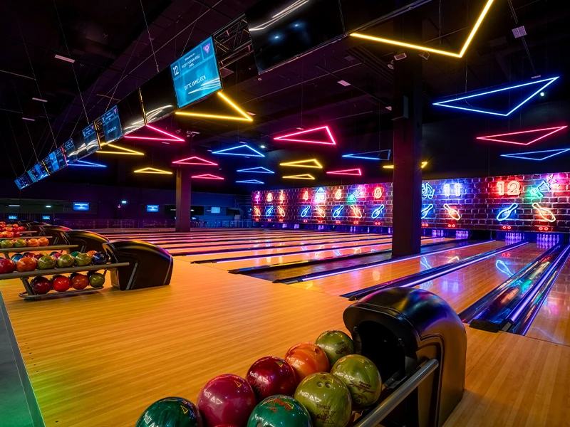 Moderne Bowlingbahn mit bunten Neonlichtern und verschiedenen Bowlingkugeln in einem stilvollen Ambiente.