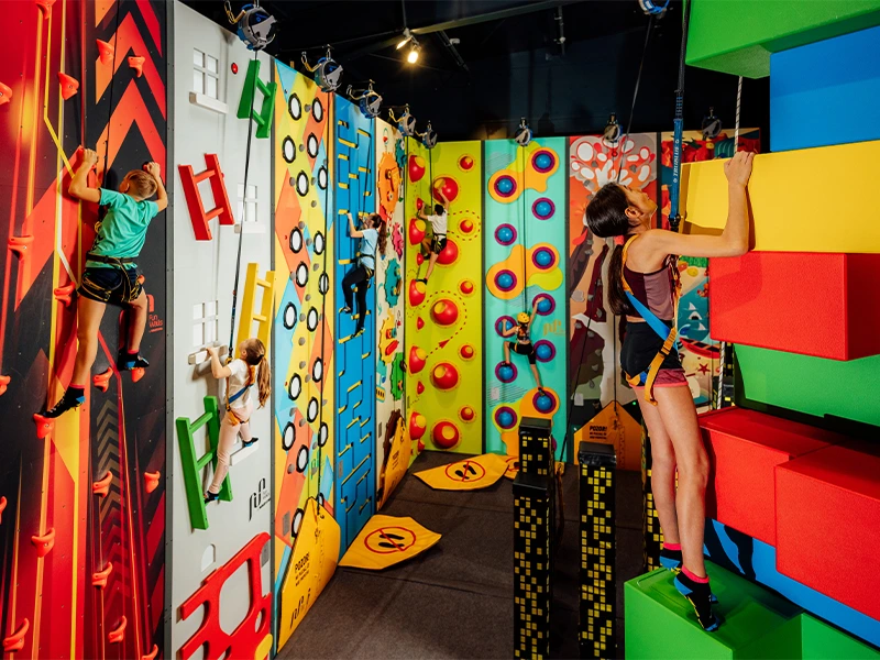 Bunte Kletterwände in einer Indoor-Kletterhalle mit Kindern, die verschiedene Kletterrouten meistern.