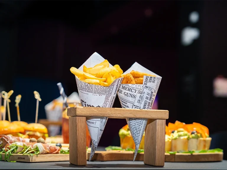 Frittierte Snacks in Papiertüten auf einem Holzständer, umgeben von verschiedenen appetitlichen Speisen.
