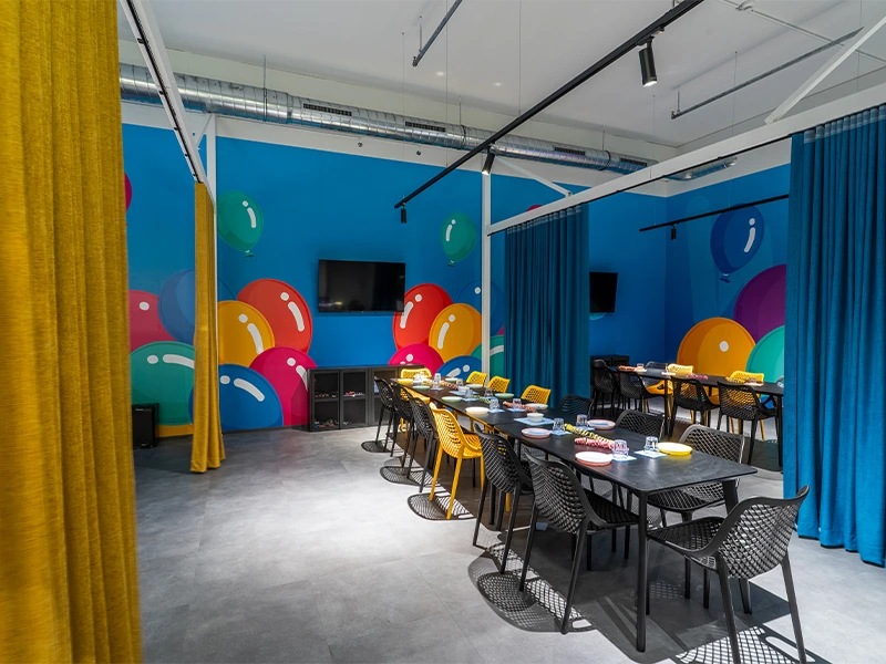 Bunte Meetingraum mit modernen Möbeln, großen Tischen und lebendiger Wandgestaltung für kreative Veranstaltungen.