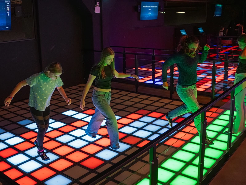 Jugendliche tanzen auf einem interaktiven LED-Boden in einer modernen Freizeitstätte. Bunte Lichter schaffen eine lebendige Atmosphäre.