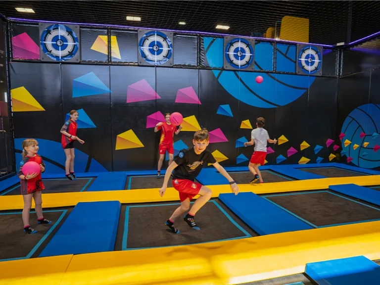 Kinder spielen in einer Trampolinhalle, werfen bunte Bälle und haben Spaß auf den Trampolinen.