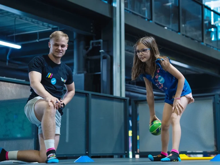 Ein Trainer beobachtet ein Mädchen, das einen Ball auf einem Sportplatz wirft. Sie üben gemeinsam Bewegungskoordination.